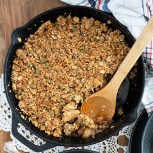 apple granola crisp in a cast iron skillet with a wooden spoon taking out a scoop.