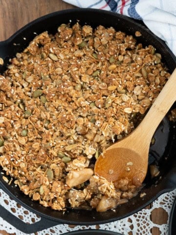 apple granola crisp in a cast iron skillet with a wooden spoon taking out a scoop.